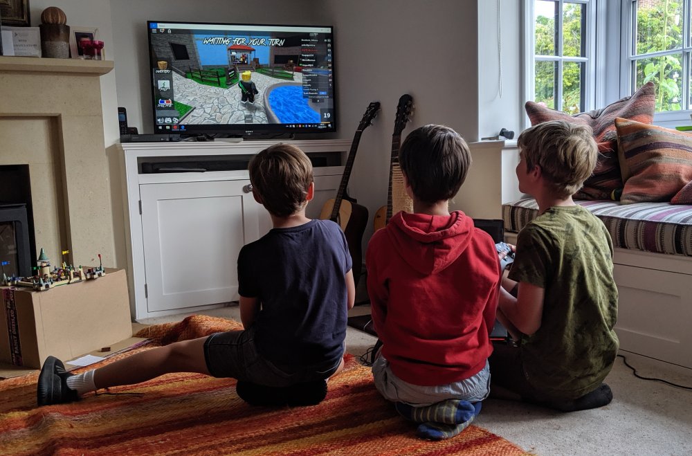 Three children playing Roblox on a TV, game screenshot in the foreground